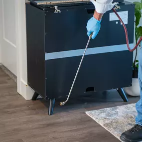 A First Line Pest Defense technician applying professional pest treatment near the base of a cabinet indoors.