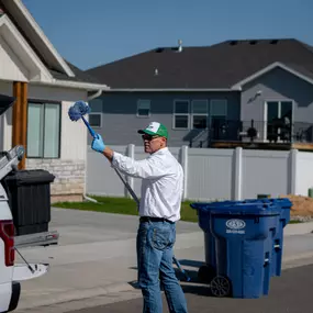 A First Line Pest Defense technician performing outdoor pest control, removing spiderwebs from a residential property.