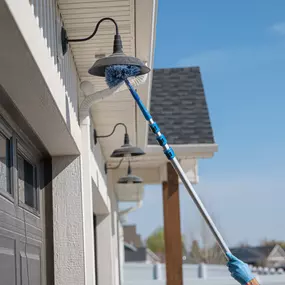 A First Line Pest Defense technician cleaning an exterior light fixture with an extension brush as part of pest prevention.