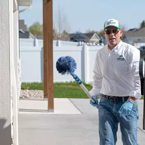 A First Line Pest Defense technician holding an exterior cleaning tool, ready to service a residential property.