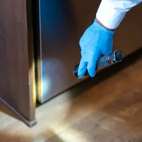 A detailed close-up showing a First Line Pest Defence technician conducting a thorough inspection. Using a flashlight, the technician meticulously checks for pests in hard-to-reach areas, like behind kitchen appliances, to ensure complete pest detection and control for our Boise clients.