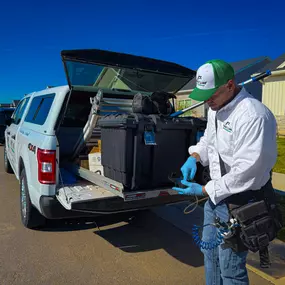 A First Line Pest Defense technician working with equipment at the back of their service truck for a pest control job.