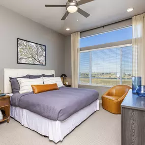 apartment bedroom has a large window and  lighted ceiling fan