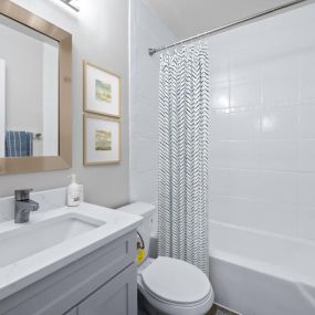 A bathroom with a white sink and toilet next to a white bathtub with a shower curtain