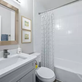 A bathroom with a white sink and toilet next to a white bathtub with a shower curtain