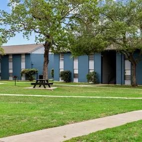 a picnic table sits in a grassy area in front of a blue building