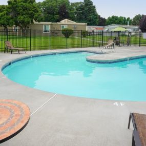 Curved outdoor pool with chairs and tables and a fence around it