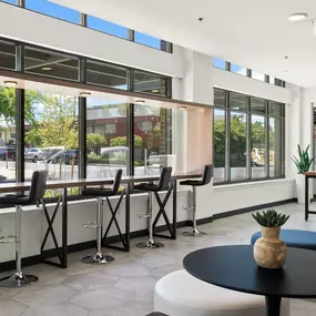 a seating area with tables and chairs in the lobby of a building with large windows