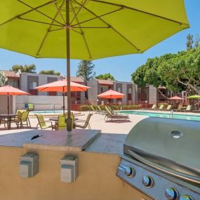 BBQ grill station with a green umbrella overlooking the pool area with tables and chair sets