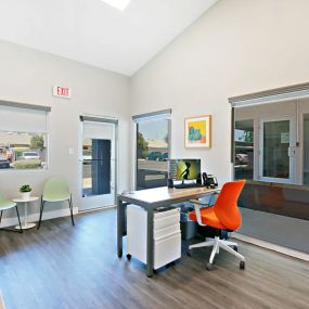 Leasing office area with plank flooring, waiting area with chairs, and a desk with an orange chair