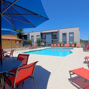Sparkling Swimming Pool with Orange Lounge Seating Surrounding, and Tables with Orange Chairs and a Blue Umbrella