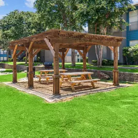 a wooden gazebo with a picnic table in the middle of a grassy area