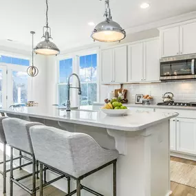 Kitchen at DRB Homes Woodleif community with white cabinets and stainless steel appliances, island with 3 bar stools.