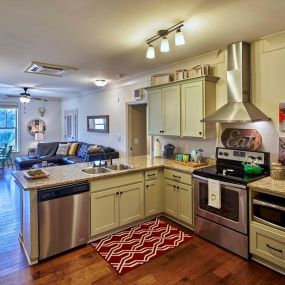 Open concept kitchen and living room with granite countertops, stainless steel appliances and hardwood flooring.