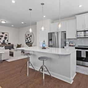 Open concept kitchen with white cabinets, island and family room in DRB Homes at Smith Farm Single Family and Townhomes community