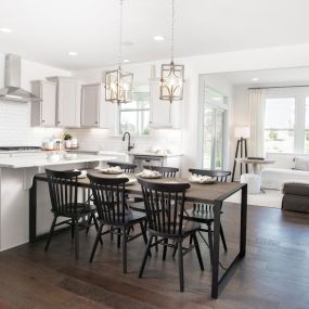 Gourmet kitchen with stainless steel appliances with white cabinets, island and dining table extension in DRB Homes at Smith Farm Single Family and Townhomes community