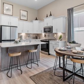 Open concept kitchen with white cabinets, stainless steel appliances and a gray island with separate dining area in DRB Homes Pleasant Falls community