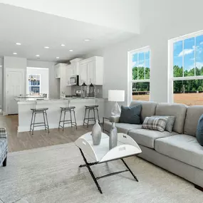 Family room with couch and two chairs open to the kitchen with white cabinets and island in DRB Homes Pleasant Falls community