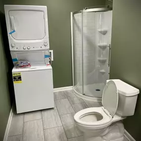 A newly installed washer and dryer in a bathroom, with a new toilets and standing shower