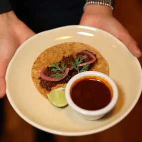 Birria (slow cooked beef) taco with sauce and a lime.