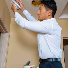 Electrician Installing Carbon Dioxide Smoke Detector In Ceiling Of Home