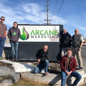 Arcane team members out in front of the business sign.