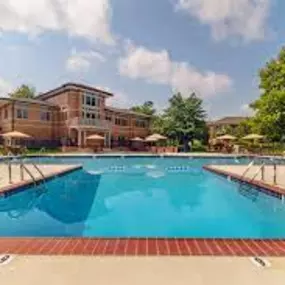 A swimming pool surrounded by lounge chairs, trees, and apartment buildings at New Kent Apartments.