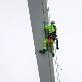 Blade repair being performed on wind turbine blade in harness in the air by worker