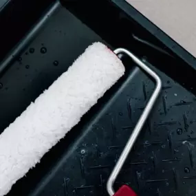 white paintbrush with red handle in black paint tray