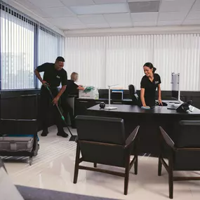 Three Anago Cleaning Systems janitorial workers cleaning an office space.