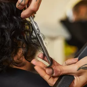 Scissors held in a tattooed hand being used to cut a client's hair.