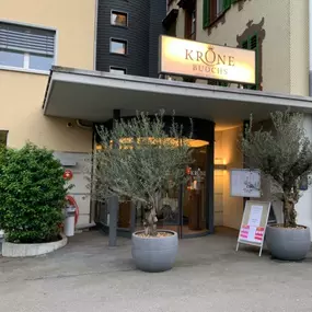 Der Eingangsbereich des Hotel Krone in Buochs. Vor der Eingangstür stehen kleine Bäume.