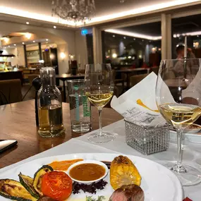 Ein Tisch, auf dem zwei Weingläser stehen und ein Teller mit Essen. Das Restaurant im Hotel Krone in Buochs.