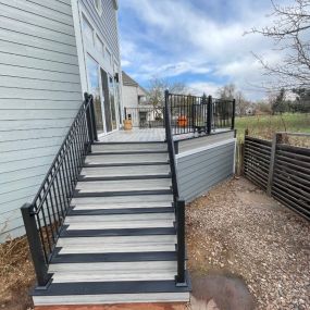 A triangle shaped composite deck with a staircase coming off the side of the deck. Deck has steel railings with ADA compliant handrail on stairs. The deck is enclosed around the underside of the deck with a wall of siding to keep animals out.