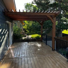 A backyard deck with black steel railings and composite decking. A 10 x 10 Full rough Cedar pergola rests on top.