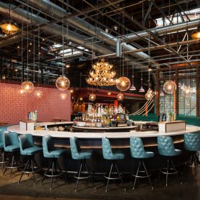 This image showcases the circular bar at Punch Bowl Social, featuring teal bar stools and modern industrial lighting. The space combines sleek decor with a laid-back, social atmosphere perfect for gatherings.