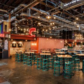 This photo showcases the open seating area at Punch Bowl Social, complete with dartboards, neon signs, and vibrant green stools. The eclectic decor and warm lighting create an inviting space for fun and socializing.