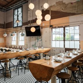 This photo highlights the rustic yet stylish dining area of Punch Bowl Social, featuring large wooden communal tables and globe pendant lighting. The exposed walls and floor tiles give the space a trendy, urban vibe.