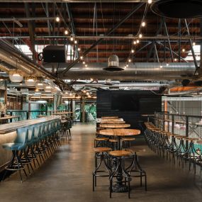 This image captures the upper-level seating area at Punch Bowl Social, featuring a long bar with teal stools and wooden tables. The industrial-style lighting and open layout offer a modern, social environment.