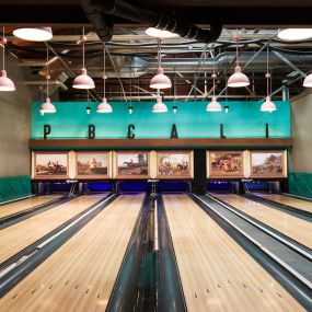 This photo features the bowling lanes at Punch Bowl Social, complete with vintage-style paintings and modern pendant lighting. The bright and inviting setup adds charm to the bowling experience.