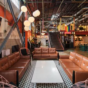 This image highlights a cozy lounge area at Punch Bowl Social with brown leather sofas and unique checkered flooring. The modern decor and exposed industrial elements create a comfortable yet stylish space.