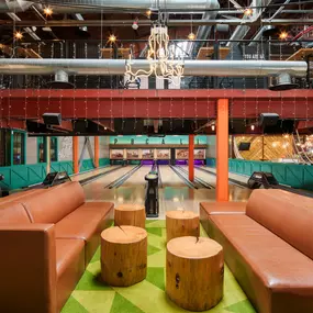 This image shows the stylish bowling alley at Punch Bowl Social, complete with leather seating and neon chandeliers. The inviting atmosphere is perfect for both bowling and socializing.