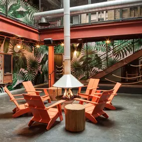 This photo highlights an indoor fire pit lounge at Punch Bowl Social, featuring orange Adirondack chairs and tropical-themed wallpaper. The cozy atmosphere adds a fun and unique element to the space.