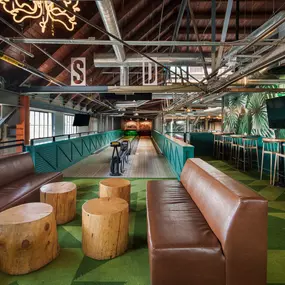 This image shows a bowling lane at Punch Bowl Social, complete with leather seating and rustic tree stump tables. The venue's combination of modern and natural elements creates a fun and stylish bowling experience.