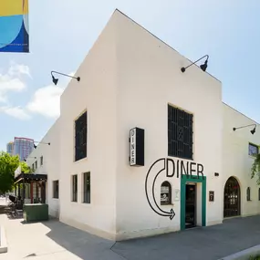 This image shows the corner view of Punch Bowl Social's Diner, featuring large windows, a minimalist white exterior, and modern signage. The stylish facade blends well with the surrounding urban environment.