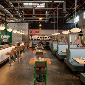 This image shows the trendy interior of Punch Bowl Social, featuring teal booths, a sleek bar, and modern hanging light fixtures. The industrial-style ceiling and retro diner-inspired bar stools add to the space's unique charm.