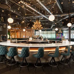 This photo showcases a circular bar at Punch Bowl Social Atlanta, with teal bar stools and modern hanging lights. The bar area is inviting and vibrant, perfect for social gatherings.