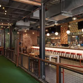 This image features an indoor game area at Punch Bowl Social Atlanta, complete with a bar, cornhole setup, and casual seating. The space is designed for fun and socializing, with a laid-back vibe.