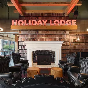 This image captures the cozy Holiday Lodge seating area at Punch Bowl Social Atlanta, complete with black leather chairs and a warm fireplace. A neon sign reading 'Holiday Lodge' adds a modern touch to the rustic decor.