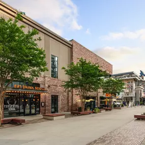 This image captures the exterior of Punch Bowl Social in Atlanta, featuring a rustic brick facade and a bold, lit-up sign that reads 'Eat Drink Social.' The surrounding area is vibrant with trees and outdoor seating.